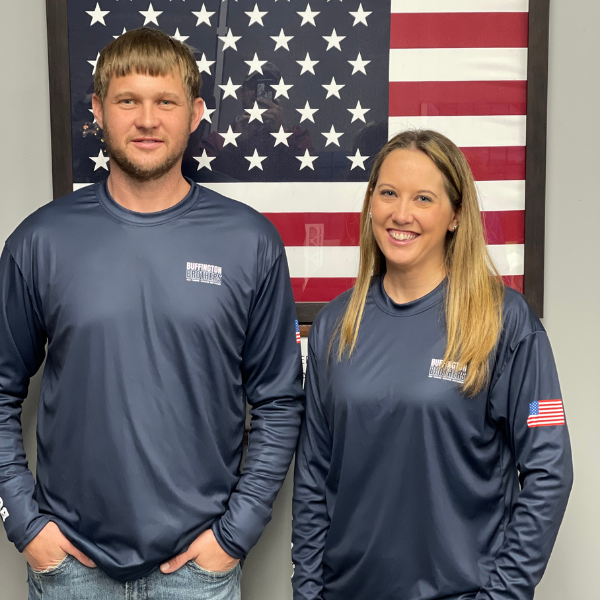 Stacy and Ryan Buffington, third generation, in matching company shirts with an American flag in the background.