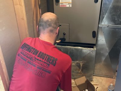 Buffington Brothers technician in a red Buffington Brothers Heating & Cooling company shirt working inside a residential furnace cabinet.